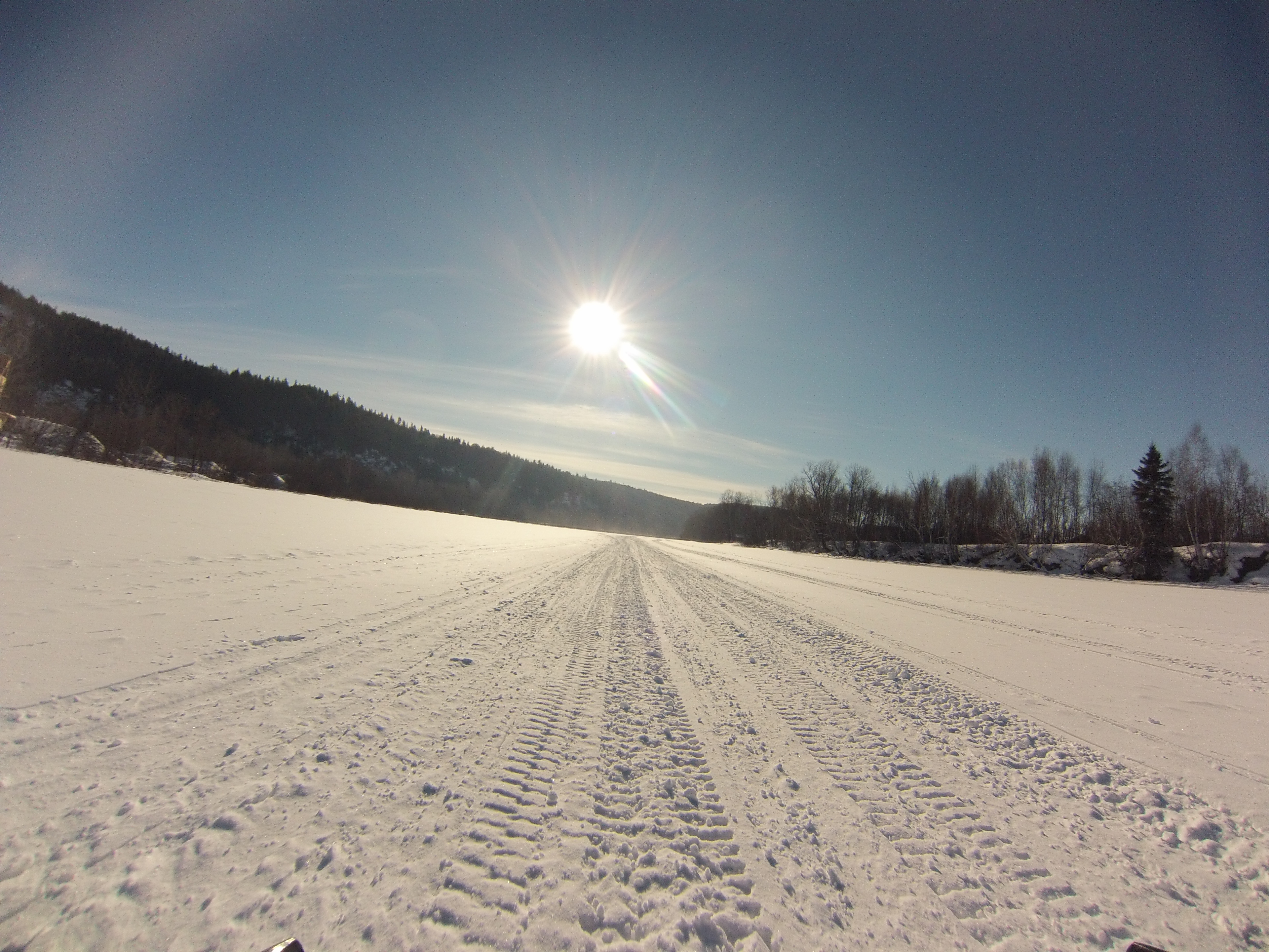 A picture of the winter sun over a frozen lake with a snowmobile track.